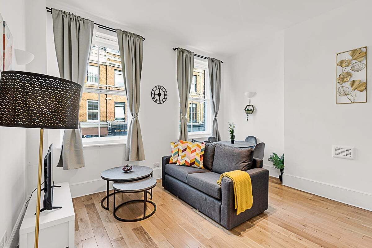 A living room with a sofa, a small round table, a lamp, and a clock on the wall.
