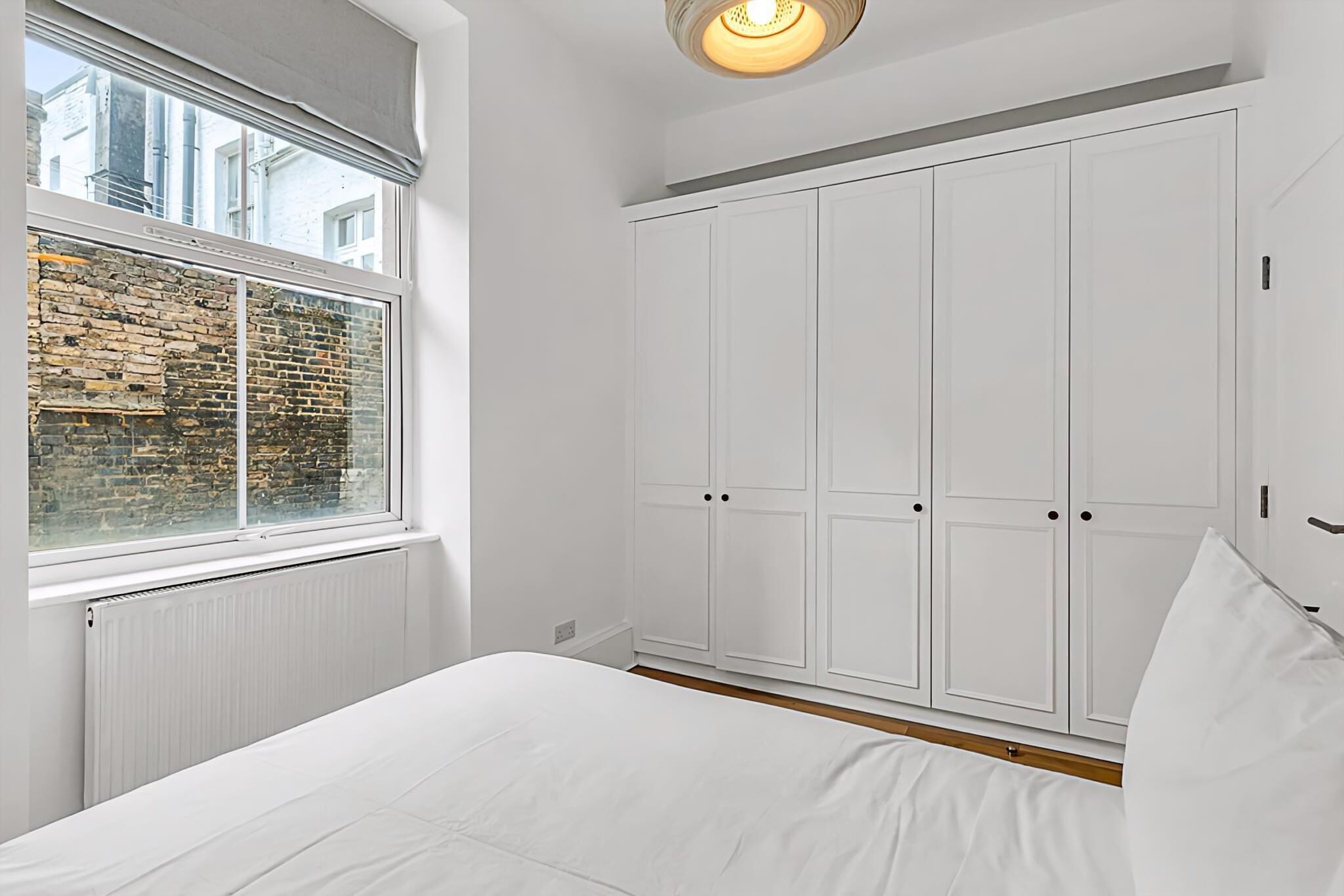 A bedroom with a large window, white wardrobe, and a bed.