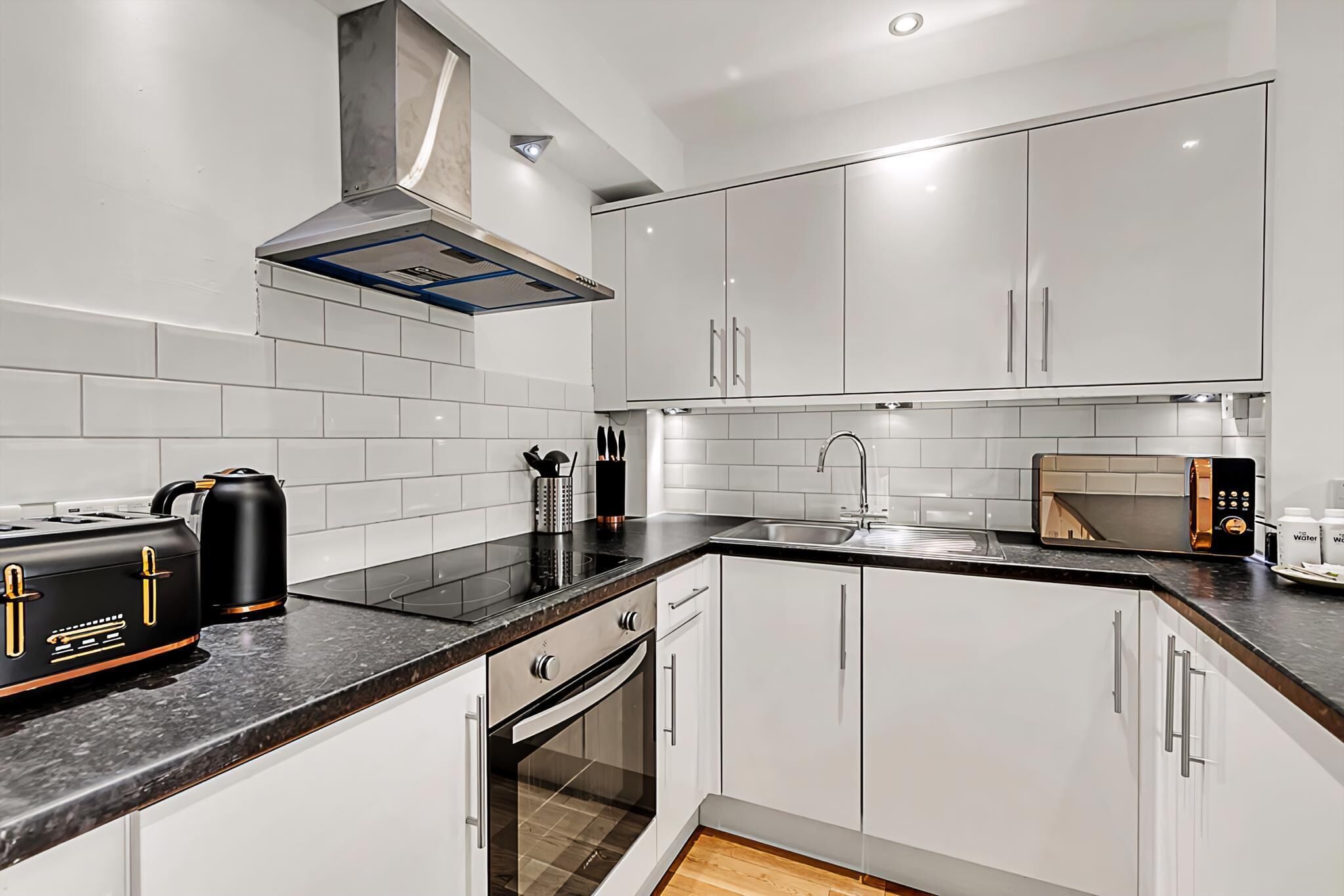 A modern kitchen with white cabinets, a black countertop, a built-in oven, a microwave, and a kettle.
