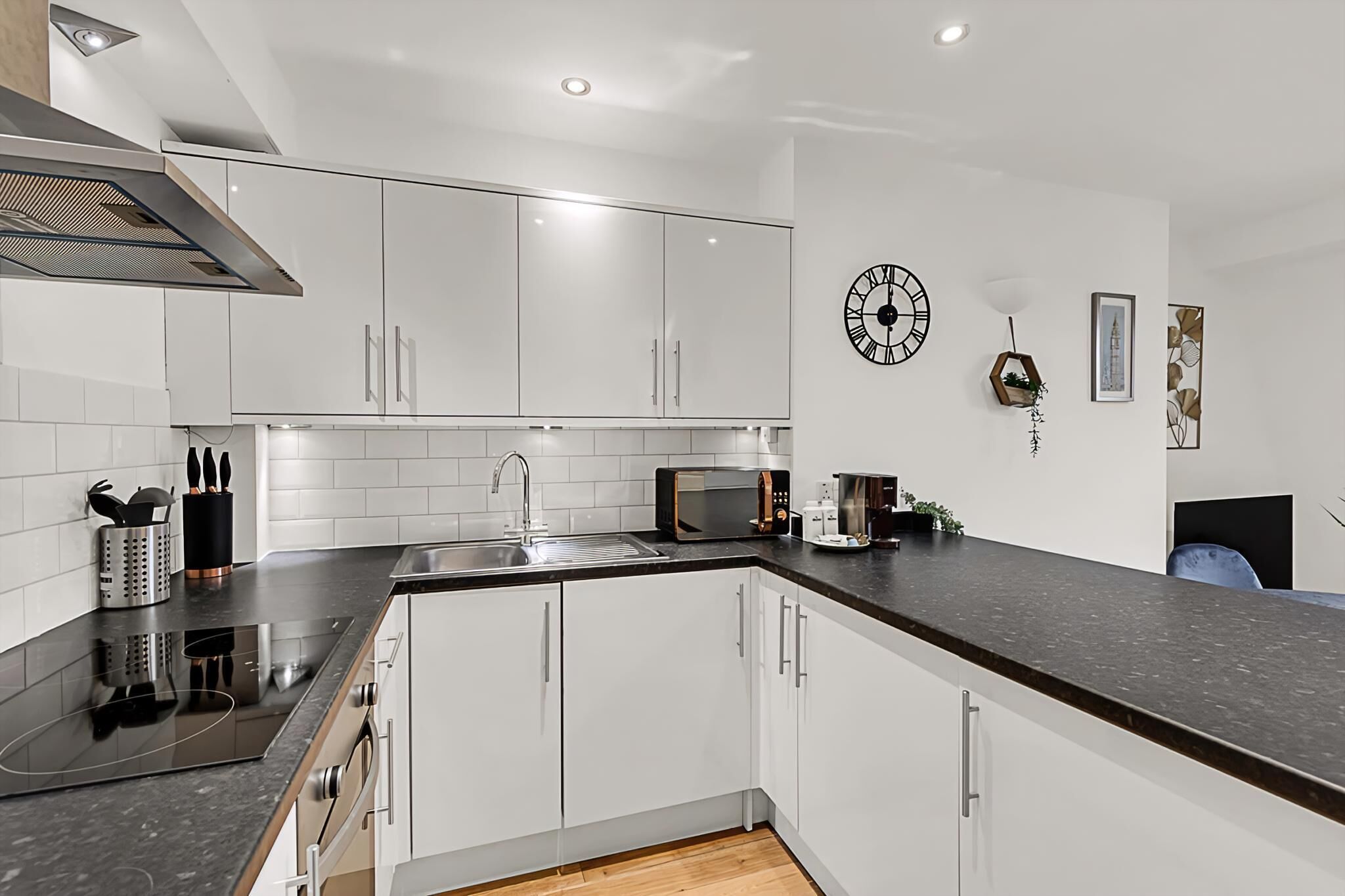 A modern kitchen with white cabinets, a black countertop, a stainless steel sink, and a microwave.