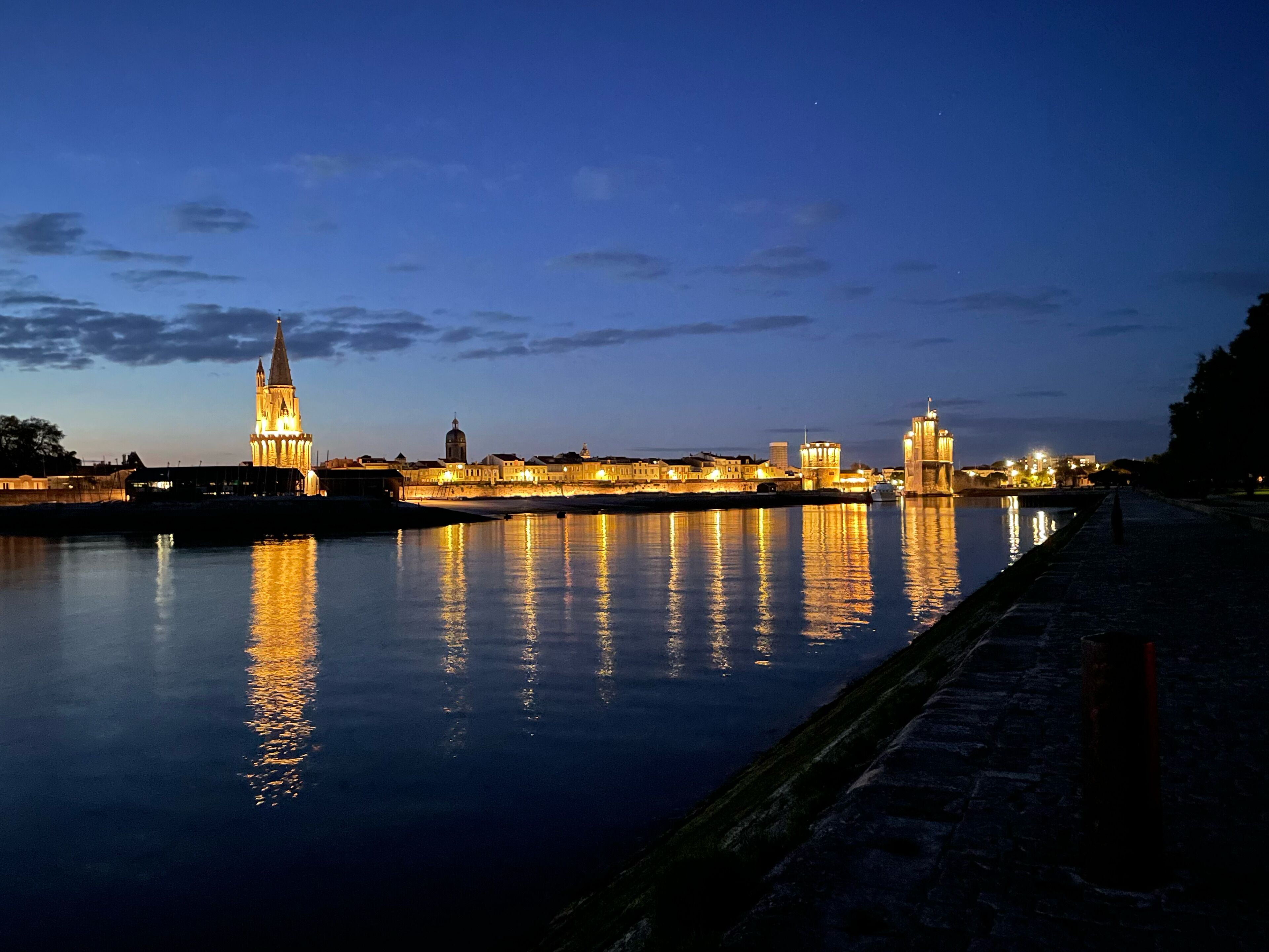 A nighttime cityscape with illuminated buildings reflecting on the water.