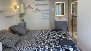 A modern bedroom with a bed, bedside tables, a mirror, and a shower area.