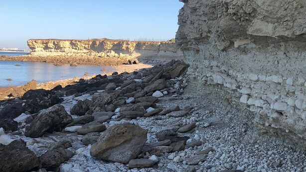 A rocky shoreline with a cliff and a clear sky.