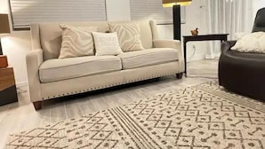 Un soggiorno con un divano color beige, un tappeto decorato e una lampada.