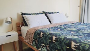 A bed with a patterned bedspread, two white pillows, a wooden nightstand with a lamp, and a wooden drawer unit. - Fun on Foam Cape Paterson (Cape Paterson)