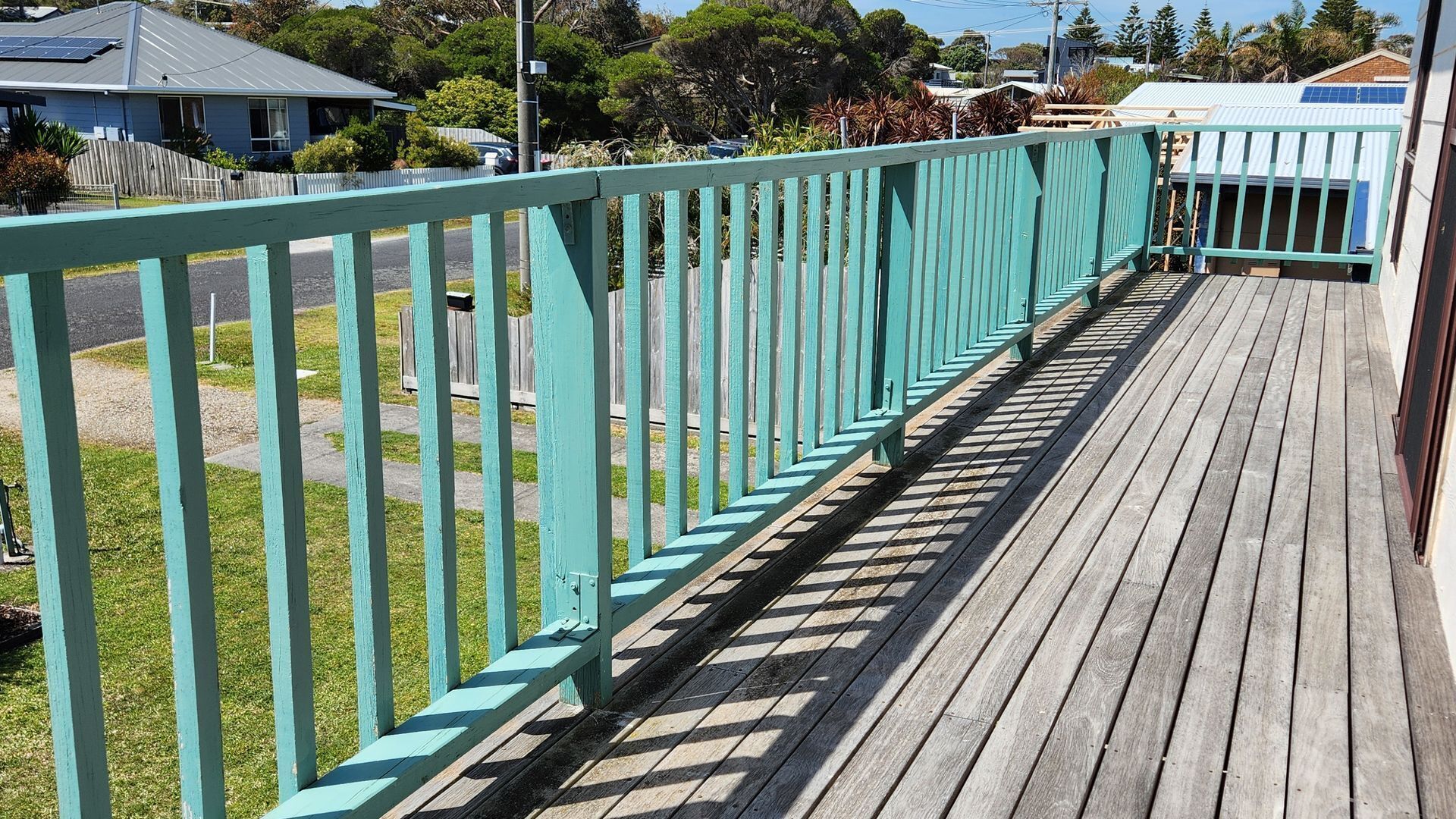 A wooden deck with a turquoise railing, leading to a building with a white exterior and solar panels on the roof.