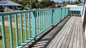 A wooden deck with a turquoise railing, leading to a building with a white exterior and solar panels on the roof. - Fun on Foam Cape Paterson (Cape Paterson)