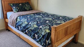 A single bed with a wooden frame, a dark blue bedspread with a leaf pattern, and a matching pillow. - Fun on Foam Cape Paterson (Cape Paterson)