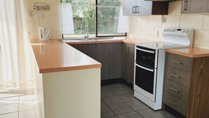 A kitchen with a built-in oven, a sink, and a window with curtains. - Fun on Foam Cape Paterson (Cape Paterson)