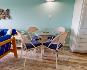 A dining area with wicker chairs, a glass table, and a blue sofa.