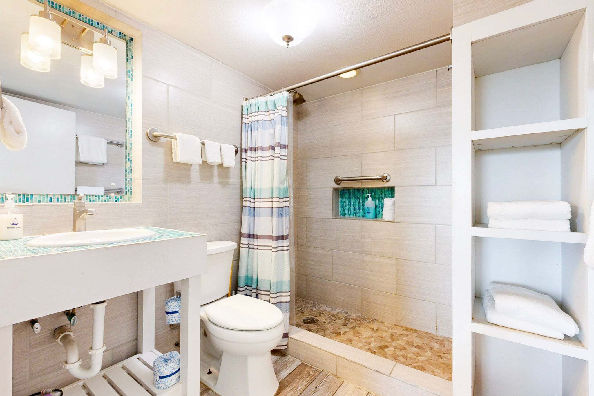 Une salle de bain équipée d’un lavabo, de toilettes, d’une douche et d’étagères où sont rangées les serviettes.