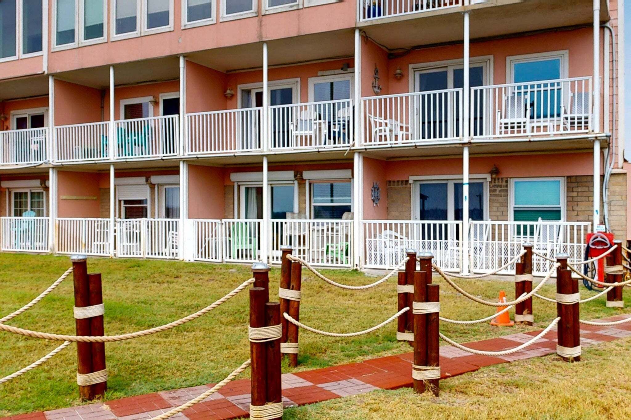 A multi-story residential building with balconies, a gated entrance, and a paved pathway.