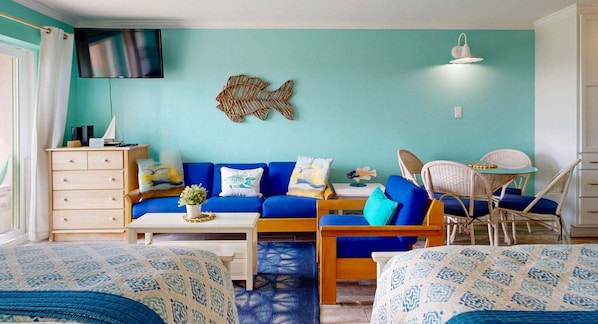 A room with a blue sofa, a wooden coffee table, a white dresser, wicker chairs, and a small table with a white lamp. - Walk to Sandfest, Shared Pools, Boardwalk to the Beach (Port Aransas)