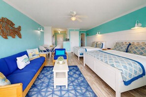 A room with a blue sofa, a bed with patterned bedding, a white coffee table, and a ceiling fan.