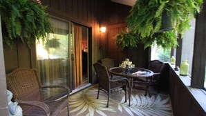 Un patio techado con mobiliario de mimbre, una puerta de cristal y helechos colgantes.