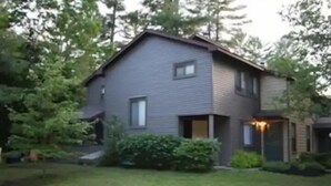 Una casa de dos pisos con revestimiento oscuro, un porche delantero y un césped bien cuidado.