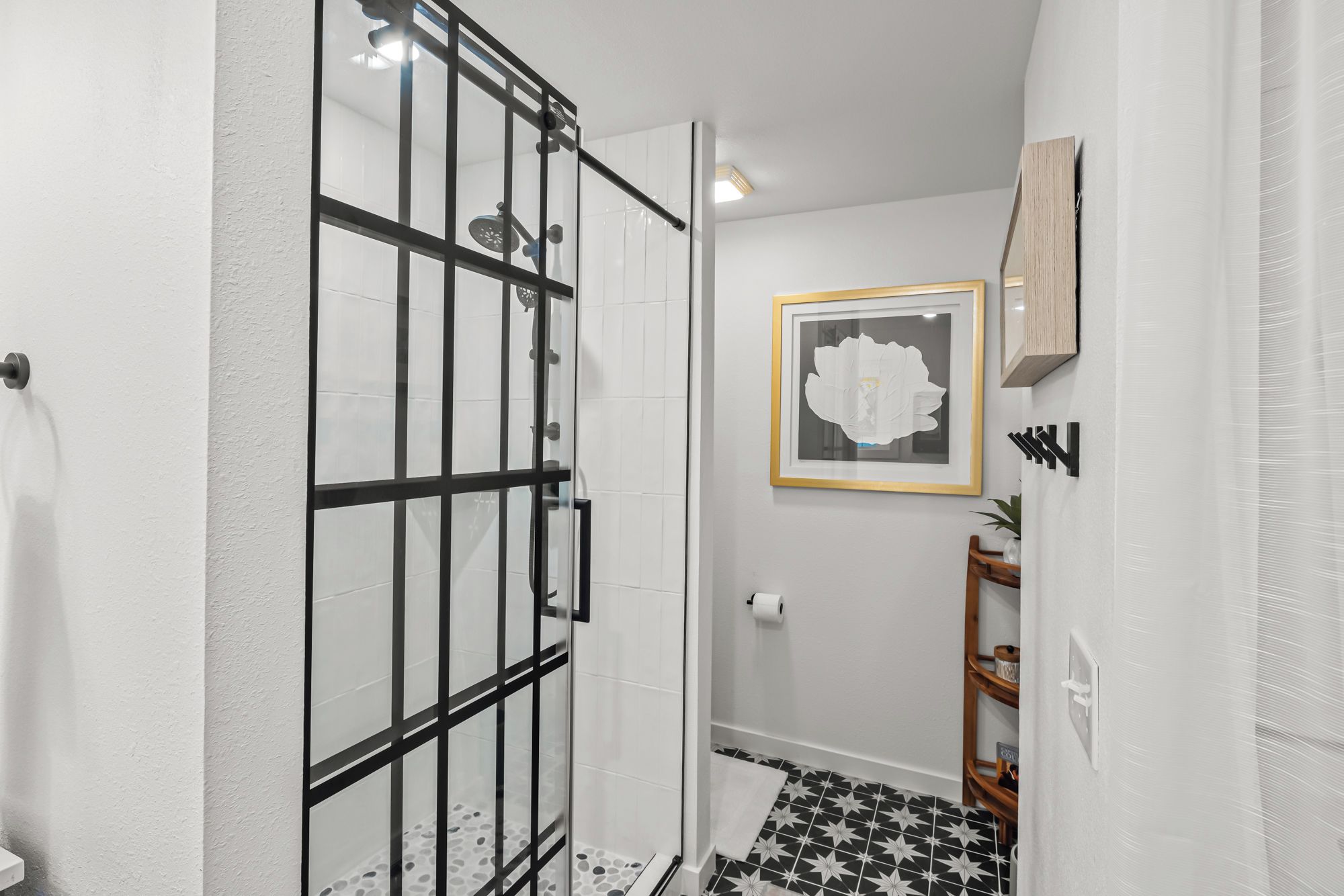 A bathroom with a glass shower enclosure, a framed artwork on the wall, and a patterned floor.