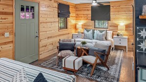 Een knus houten blokhutkamer met een bed, twee stoelen, een tafeltje en een nachtkastje.