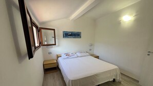 Une chambre d’hôtel comprenant un lit, des tables de chevet, une commode, un miroir, une lampe fixée au mur et un tableau encadré.
