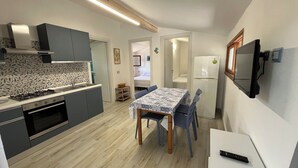 Une cuisine compacte dotée d’appareils électroménagers modernes, un coin repas avec une nappe à motifs et un téléviseur fixé au mur.