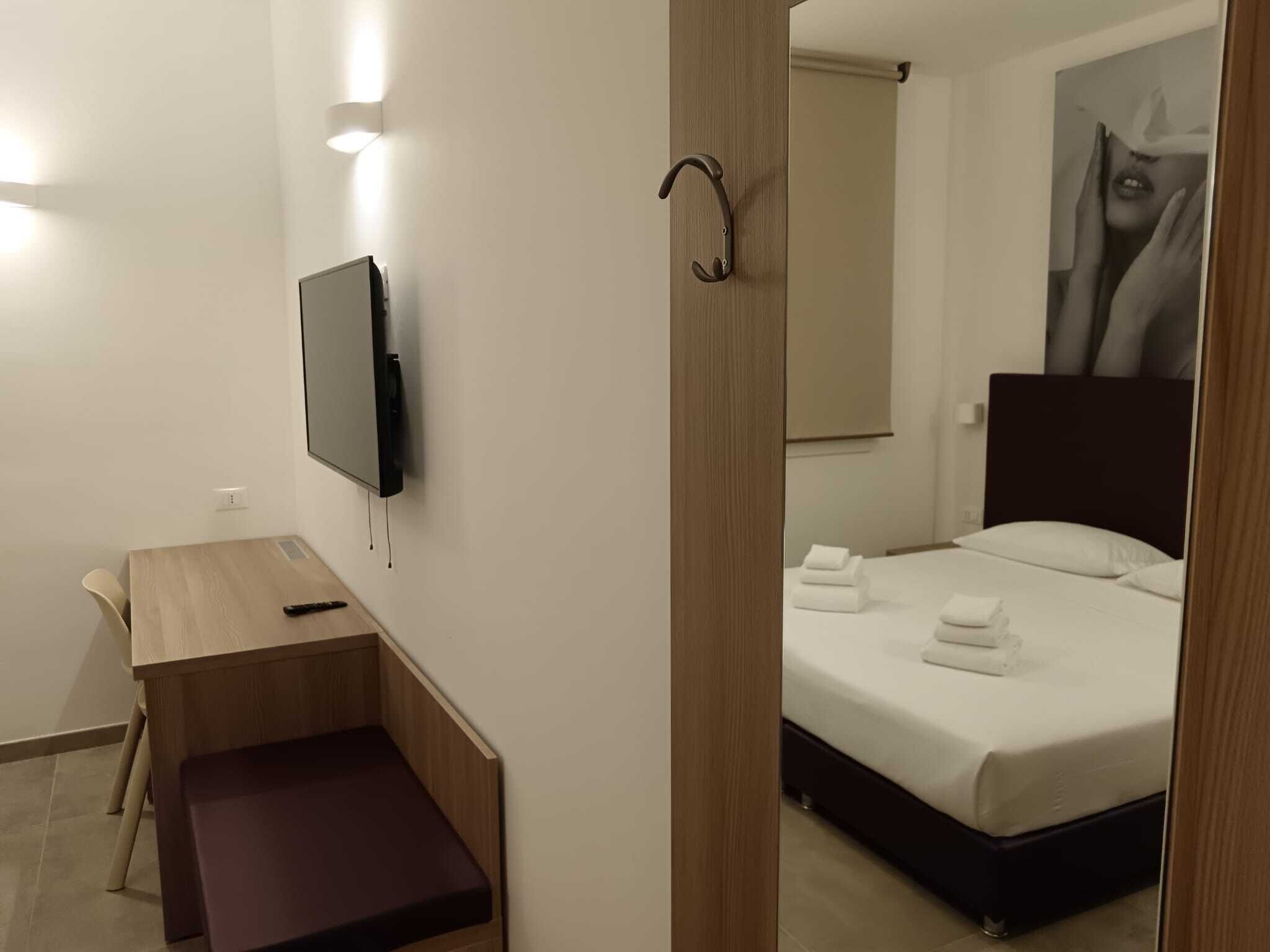 Une chambre d’hôtel avec un lit, un bureau, une chaise, une télévision et un grand miroir.