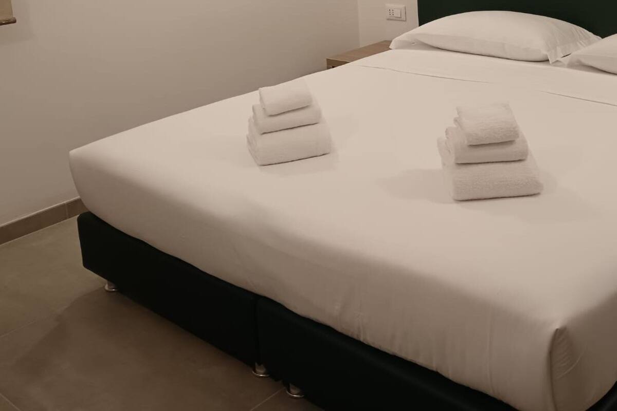 En pænt redt seng med hvide sengetøj og to sammenfoldede håndklæder på sengegavlen.