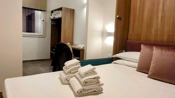 A hotel room with a neatly made bed, a wooden wardrobe, a small table with a chair, and a window. - Bertiera Rooms (Bologna)