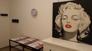 A room with a white wall, a clock, a table with informational pamphlets, and a large painting. - Bertiera Rooms (Bologna)