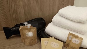 A hairdryer, a stack of white towels, and three brown paper bags with skincare products. - Bertiera Rooms (Bologna)