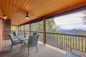 A covered outdoor seating area with a table and chairs, a brick wall, and a view of mountains.