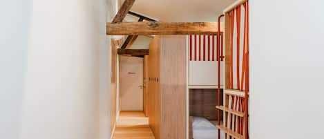 A narrow hallway with wooden flooring leading to a room with a bunk bed and a wardrobe.