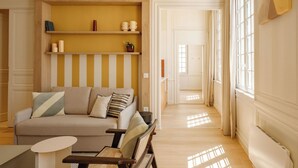 A living room with a sofa, armchairs, a small table, and a wooden shelf with decorative items. - CENTRAL (La Rochelle)