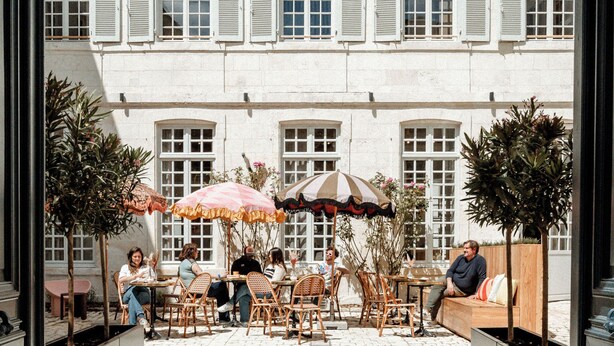An outdoor café with tables and chairs, surrounded by potted plants and umbrellas. - CENTRAL (La Rochelle)