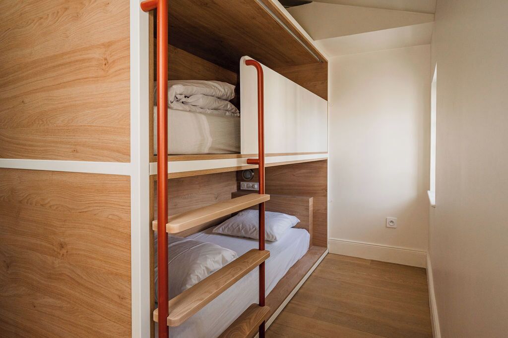 A bunk bed with wooden headboard and red metal ladder, white bedding, and a small radio on the top bunk.