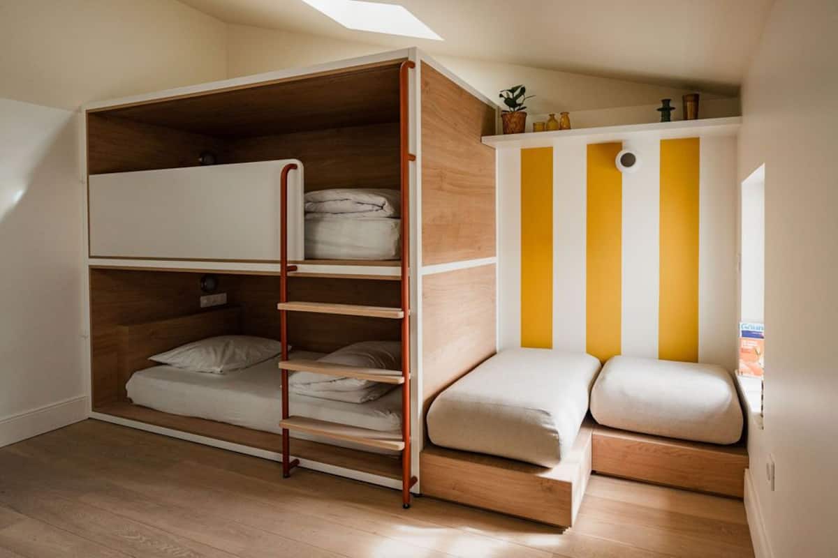 A compact room with a bunk bed, a small seating area, and a window with a view.
