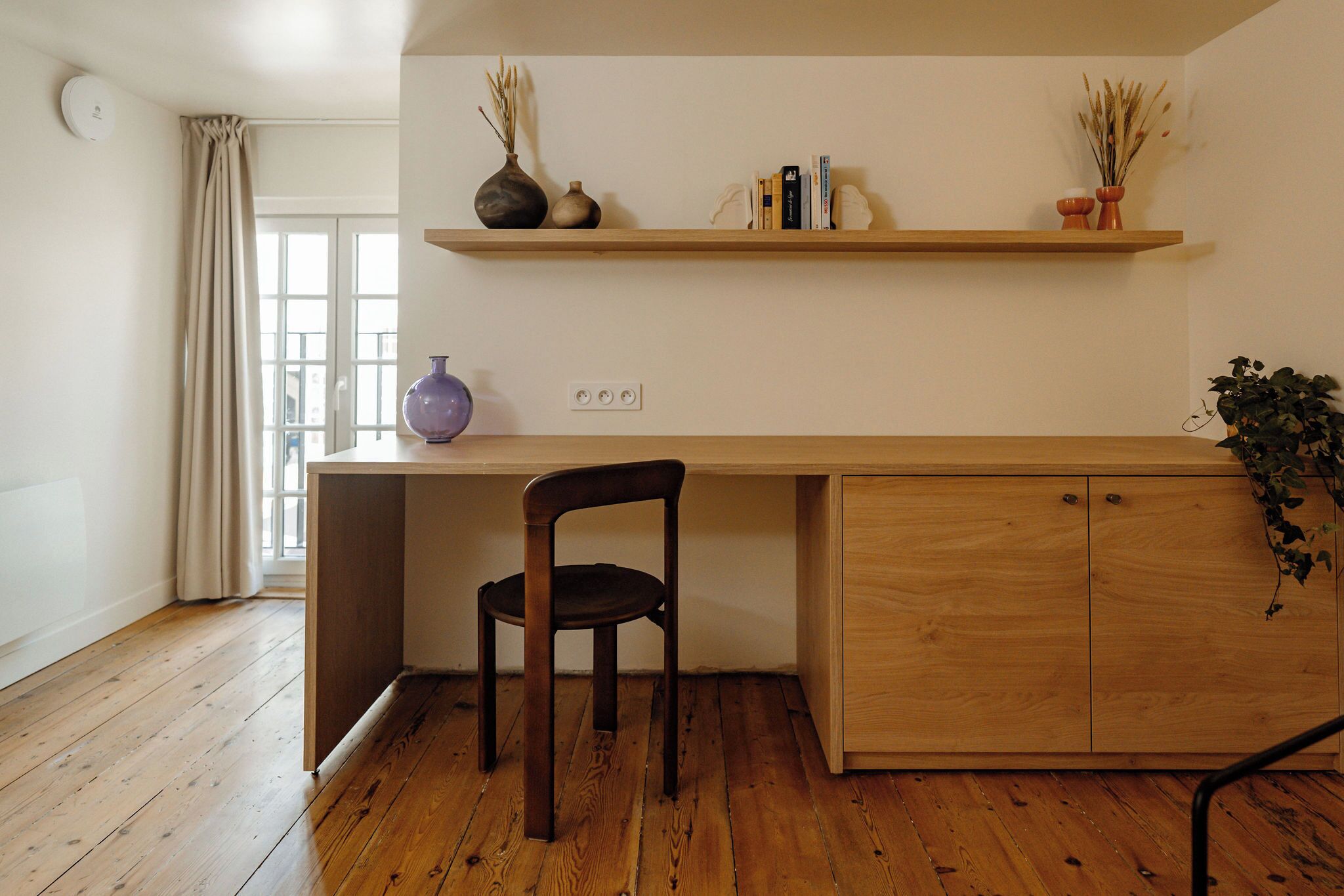 Une cuisine avec des meubles de rangement en bois, une chaise en bois de couleur sombre, un plan de travail en bois et une étagère ornée d’objets décoratifs.