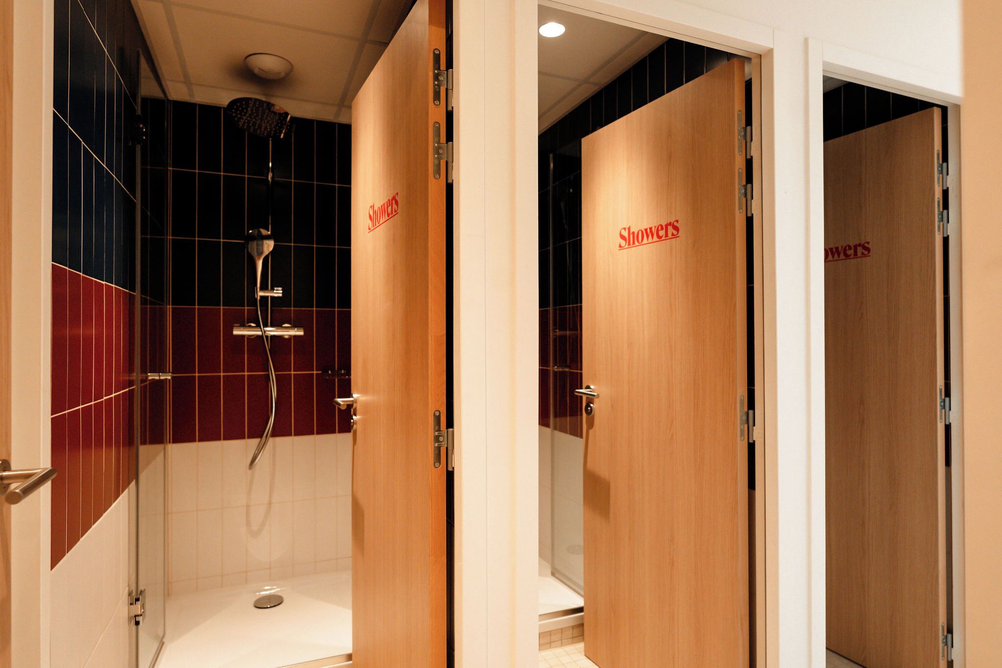 A hotel bathroom with wooden doors labeled "Showers," a glass shower enclosure, and a tiled floor.