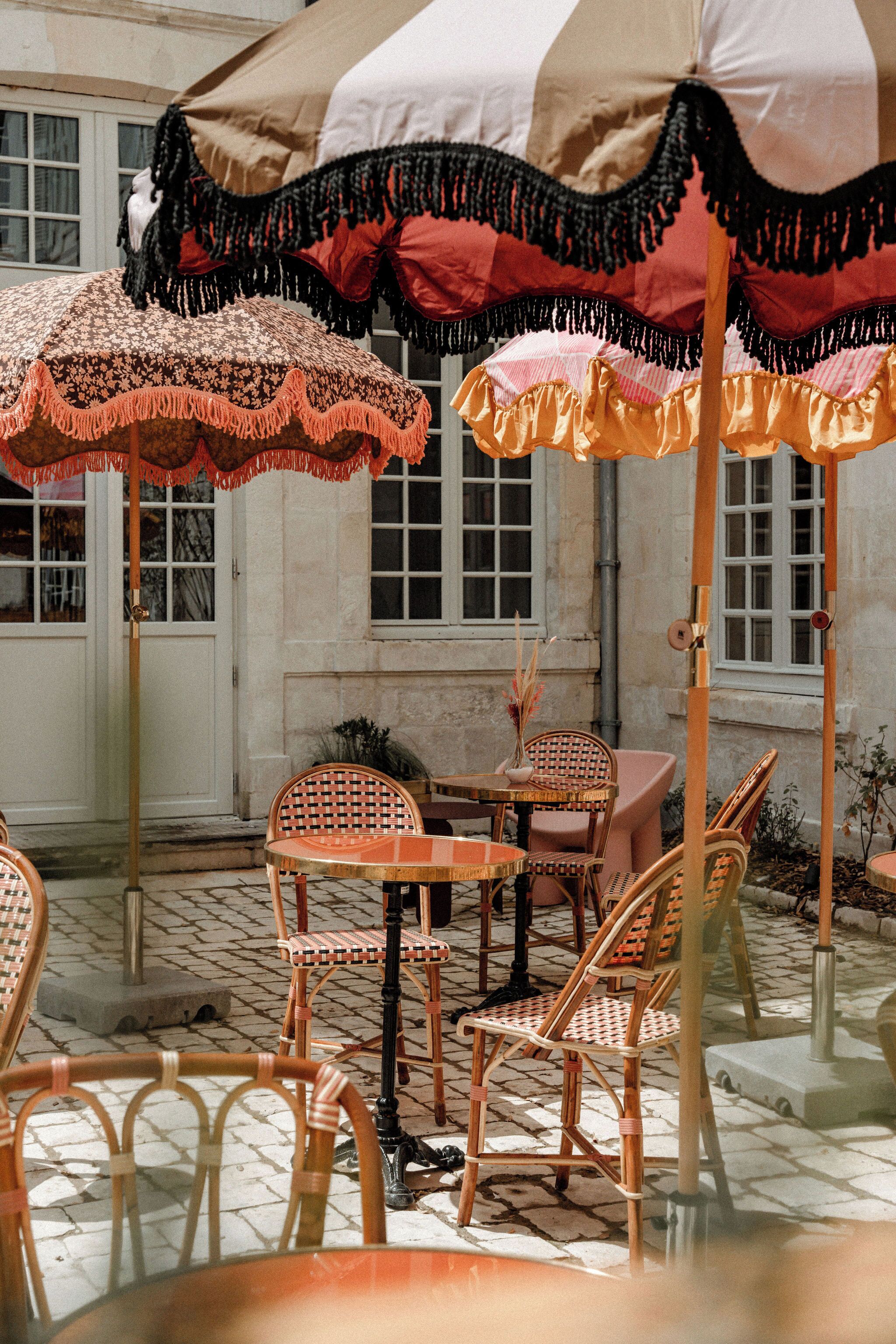 An outdoor seating area with wicker chairs and tables, covered by patterned umbrellas.