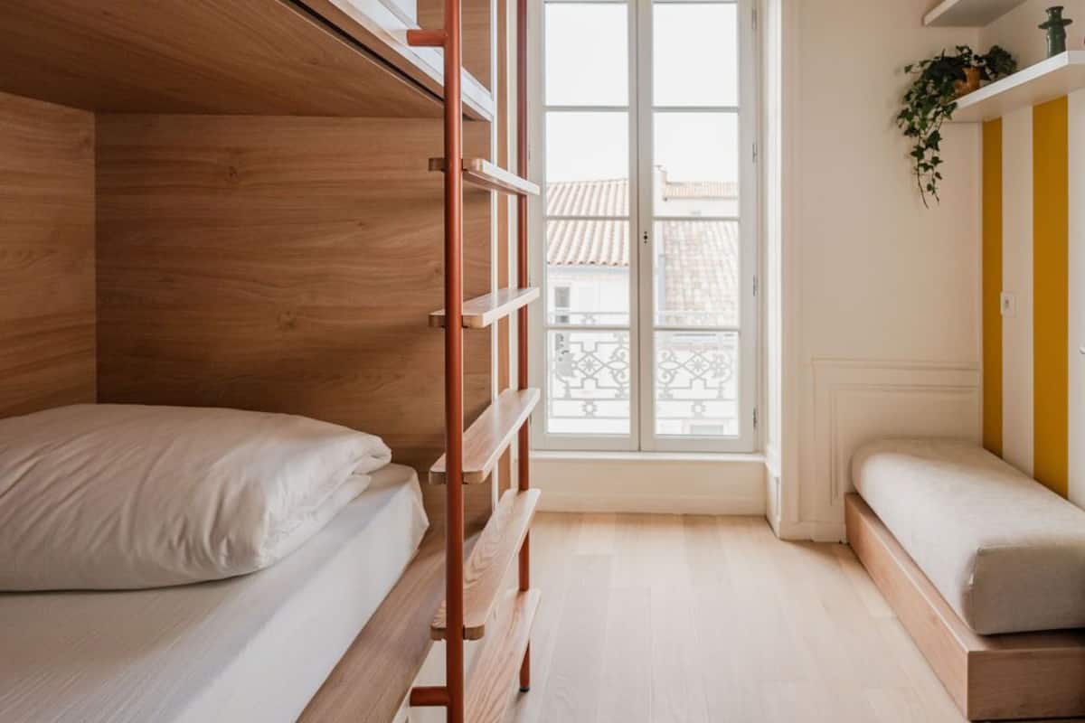 A compact room with a bunk bed, a small window, and a plant on a shelf.