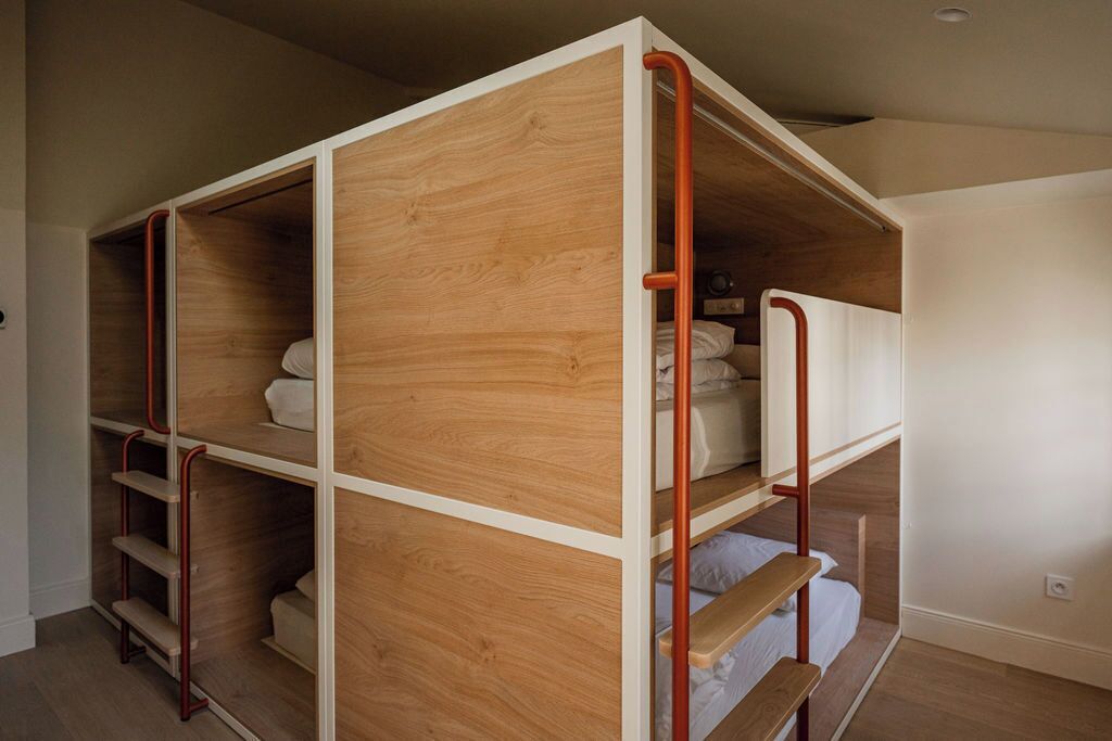 A bunk bed with wooden panels and metal railings, a white wall, and a wooden floor.