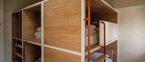 A bunk bed with wooden panels and metal railings, a white wall, and a wooden floor.