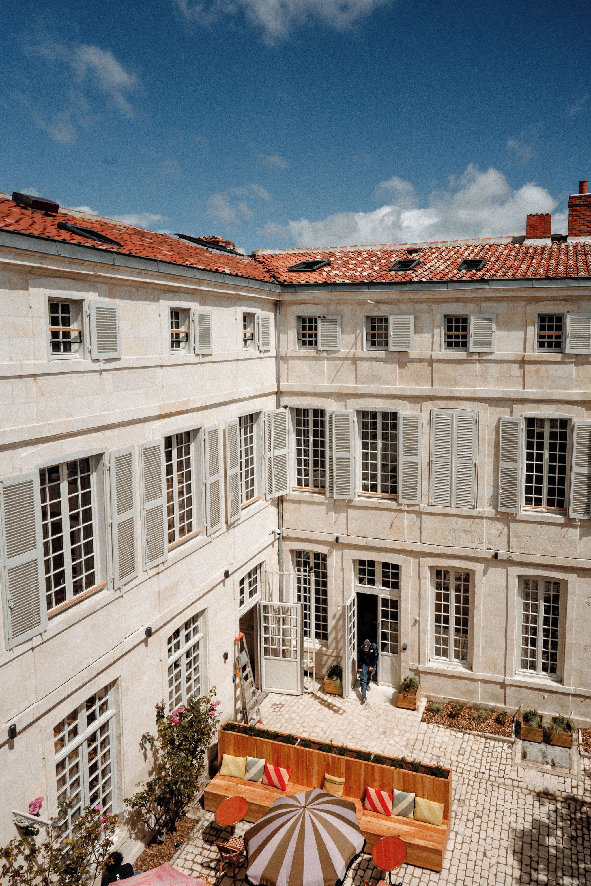 A courtyard with a tiled roof, multiple windows with shutters, and a seating area with a striped umbrella.