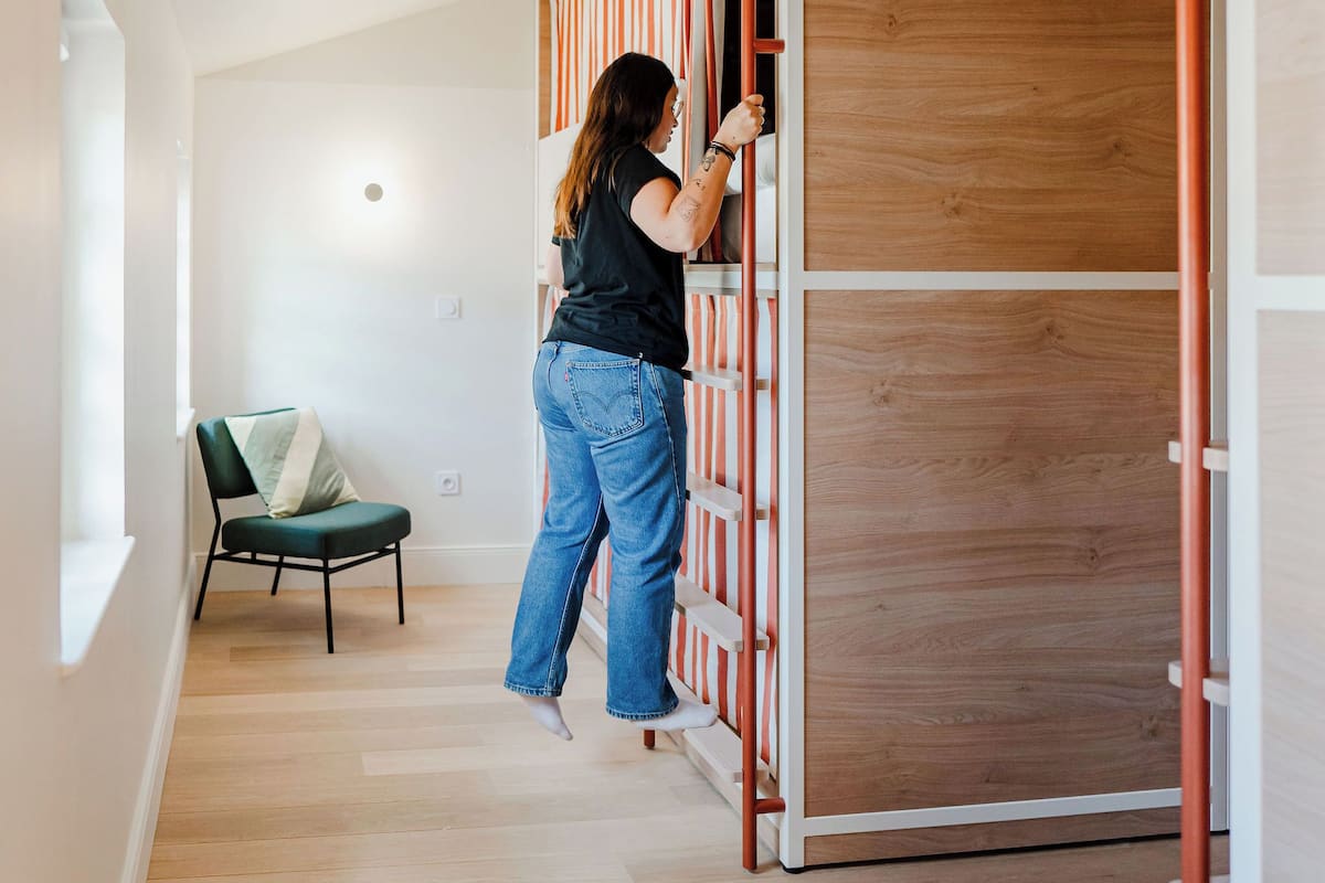 A person opening a sliding door to a room with wooden flooring and a green chair.