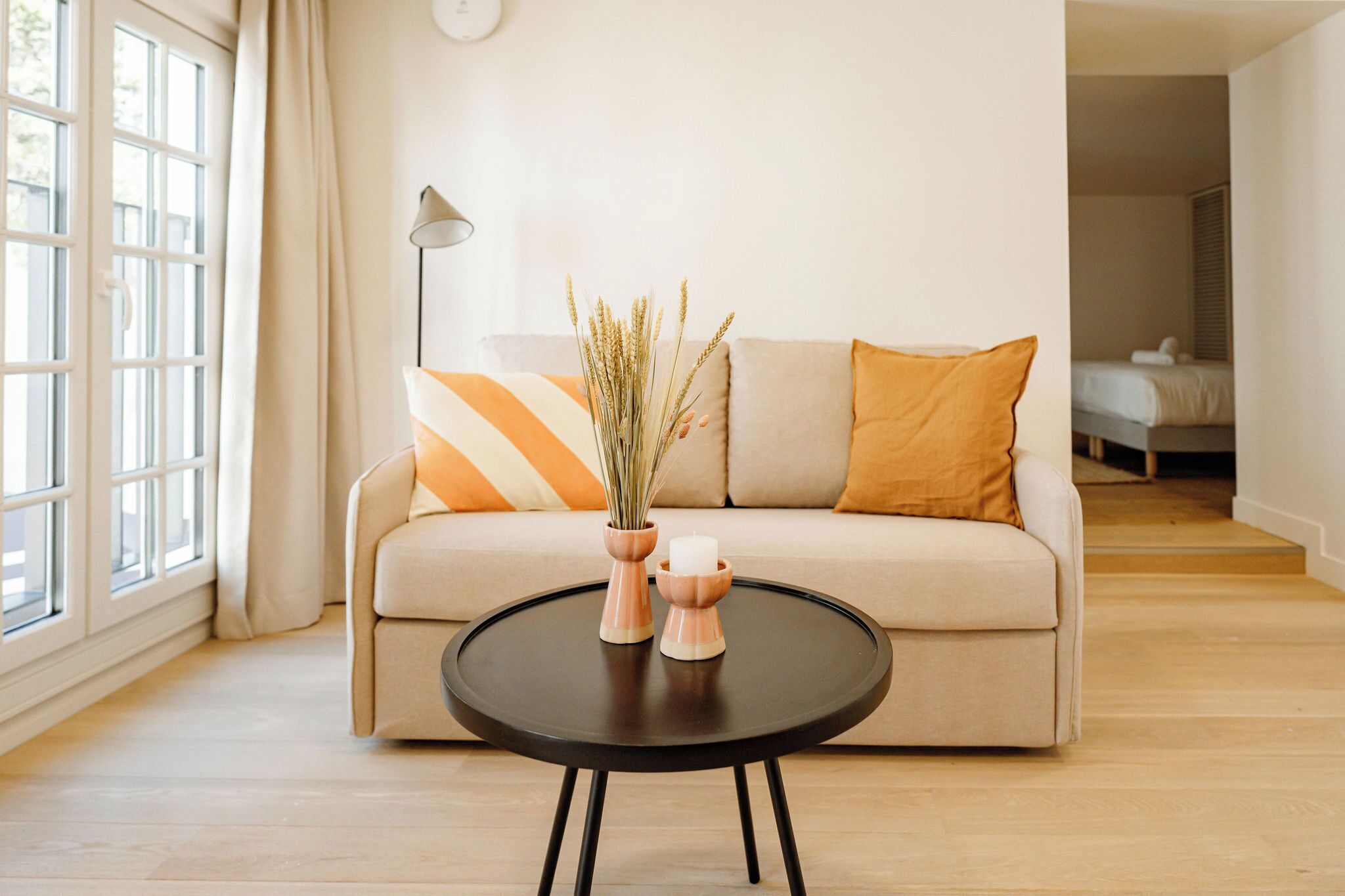 Un salon moderne avec un canapé, une table basse ronde noire et un vase contenant des plantes séchées.