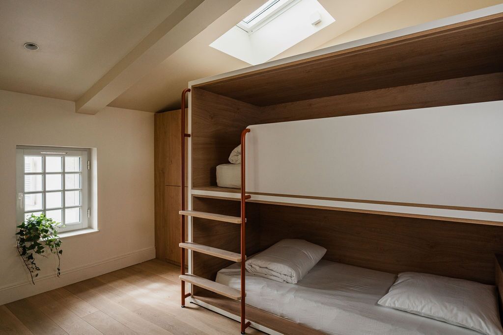 A bunk bed room with a skylight, wooden beams, and a window with a plant.