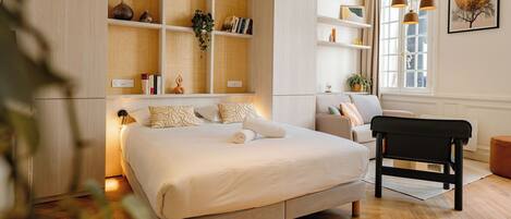 Un dormitorio con una cama grande, una mesita de noche, una silla, una estantería y una ventana con cortinas.