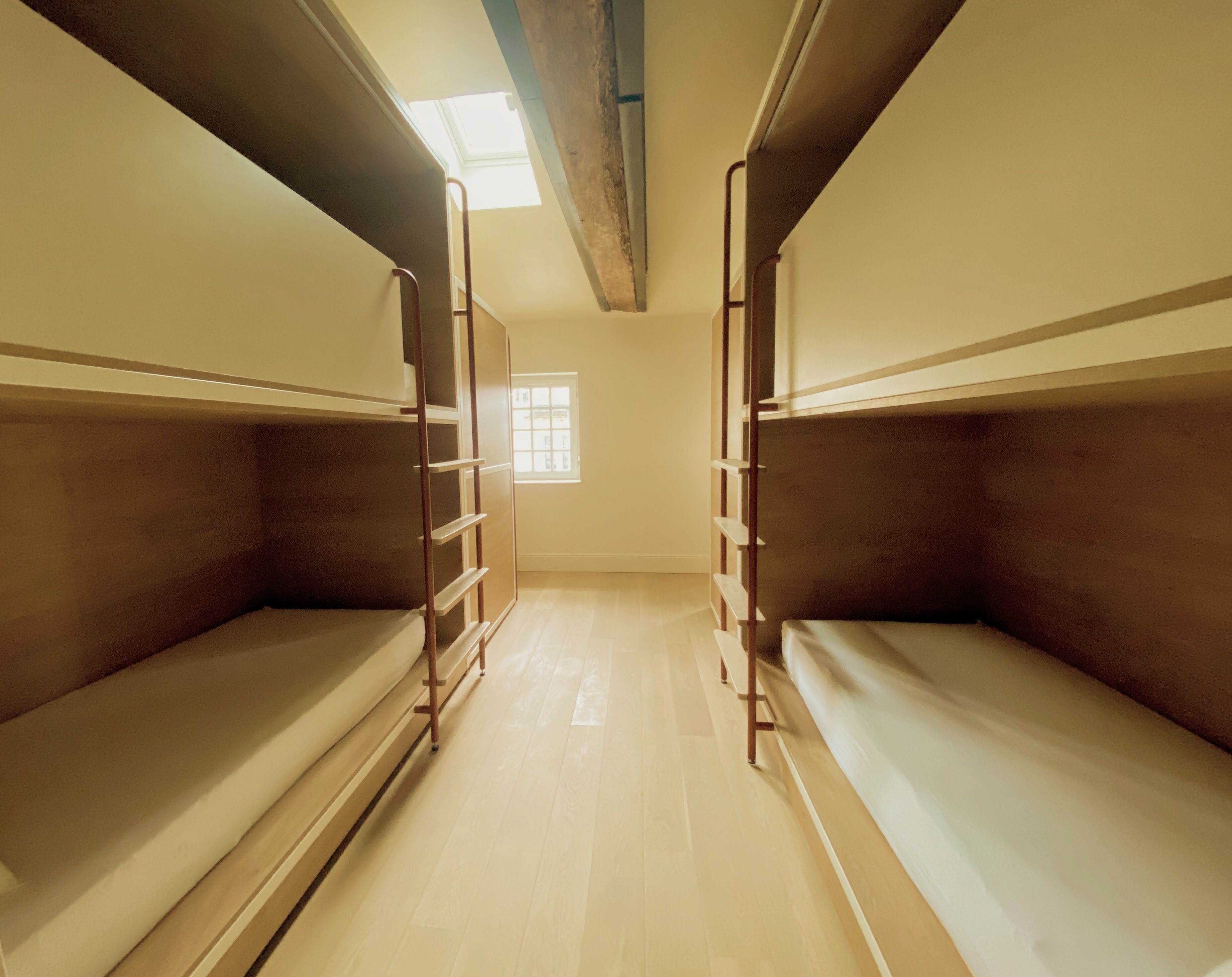 Une chambre avec deux lits superposés, des rampes en bois et un puits de lumière.