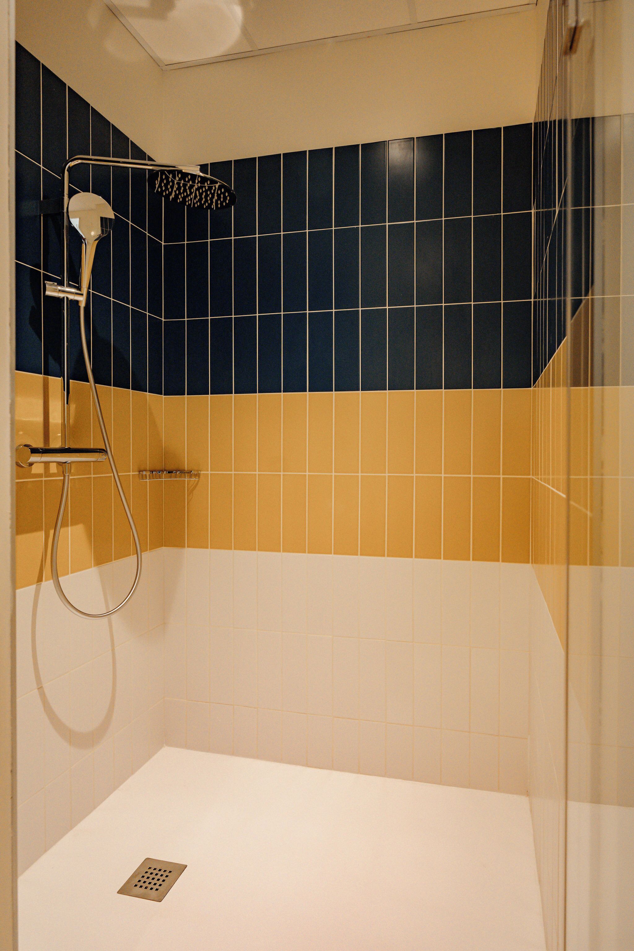 A bathroom with a shower, a handheld showerhead, and a wall-mounted faucet.