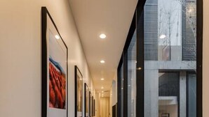 A corridor with framed artwork on the walls, a wooden floor, and a view of a building with large windows. - Majestic Heights: Retreat in La Condesa (Ciudad de México)