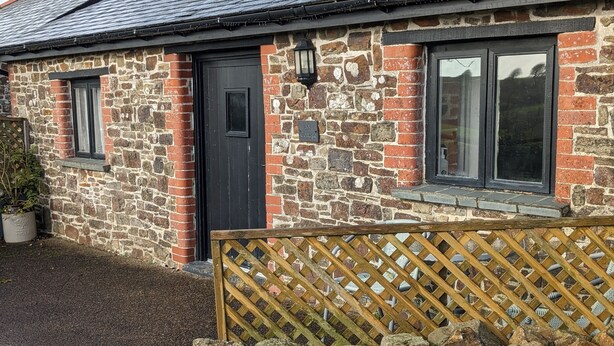 A stone house with a black door, two windows, and a wooden fence. - Elegant and Secluded 1-bed Cottage Near Bideford (Bideford)